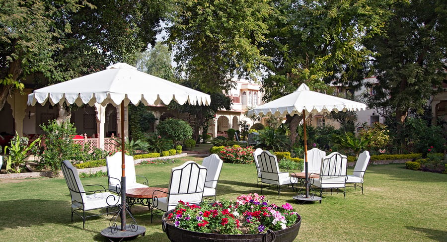 Garden lawn with white parasols, wrought-iron chairs and flower urns