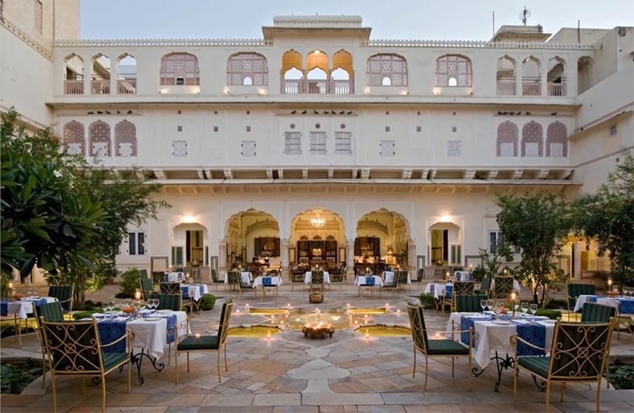 The candlelit central courtyard of Samode Haveli at dusk, tables set around a lotus fountain beneath painted arches, Jaipur