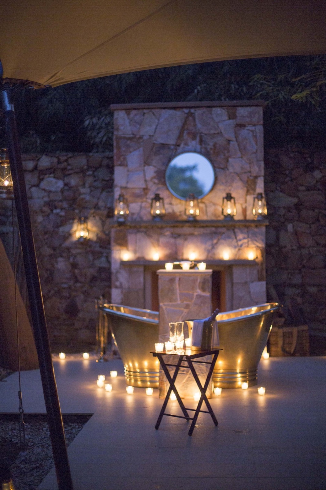Candlelit brass bathtubs under canvas at night