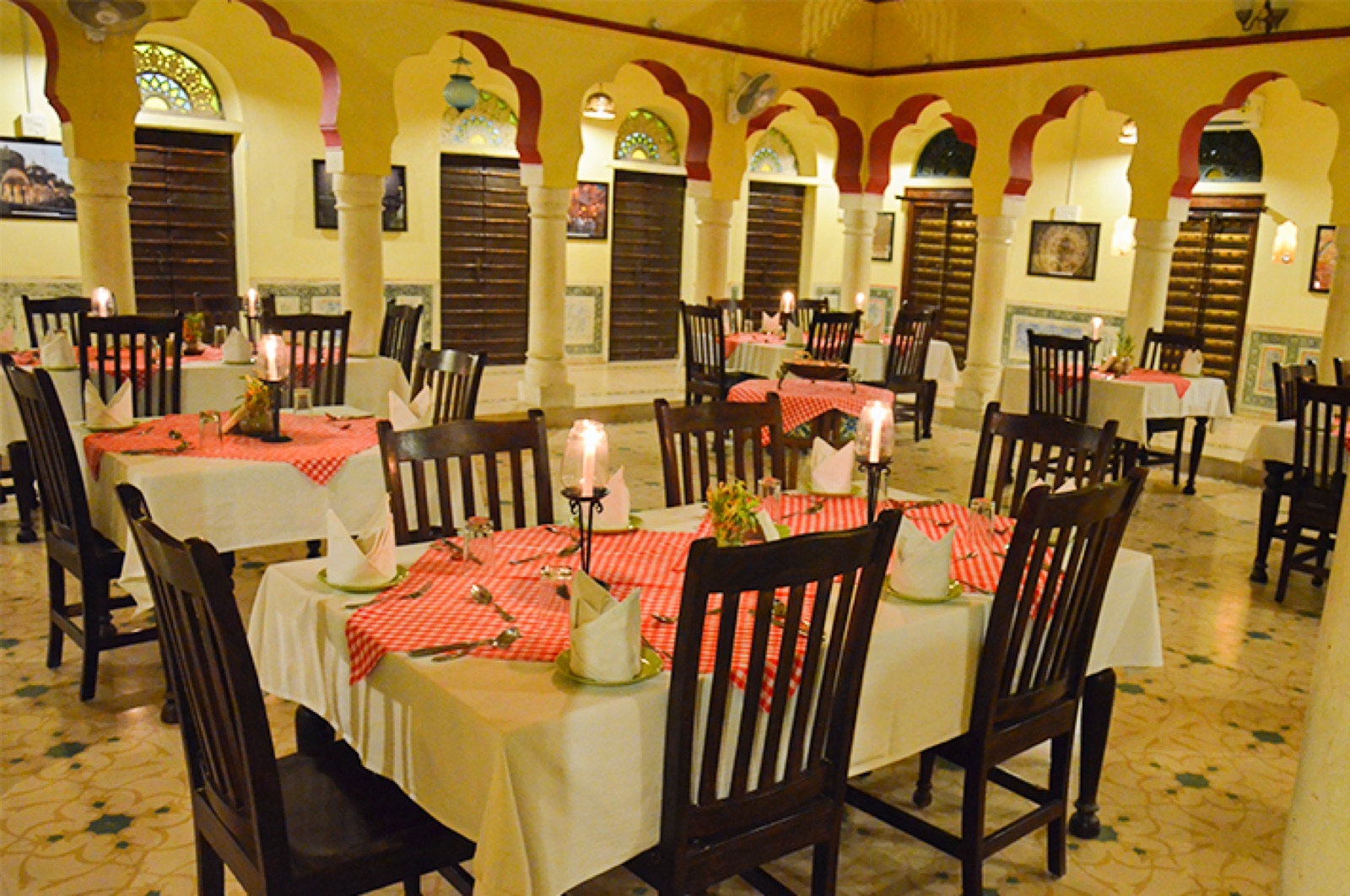 Spice Court restaurant interior: scalloped red-trimmed arches, stained-glass fanlights, patterned floor tiles, candlelit tables with white and gingham linens, no people