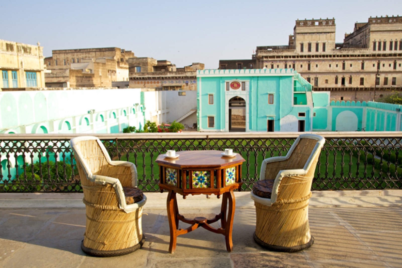 Two cane chairs and a tiled octagonal table set for tea on the rooftop terrace, overlooking the turquoise gatehouse and the weathered havelis of Churu