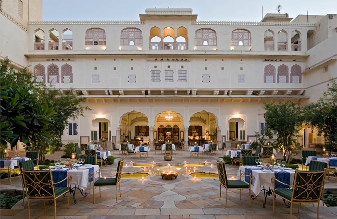 The candlelit central courtyard of Samode Haveli at dusk, tables set around a lotus fountain beneath painted arches, Jaipur